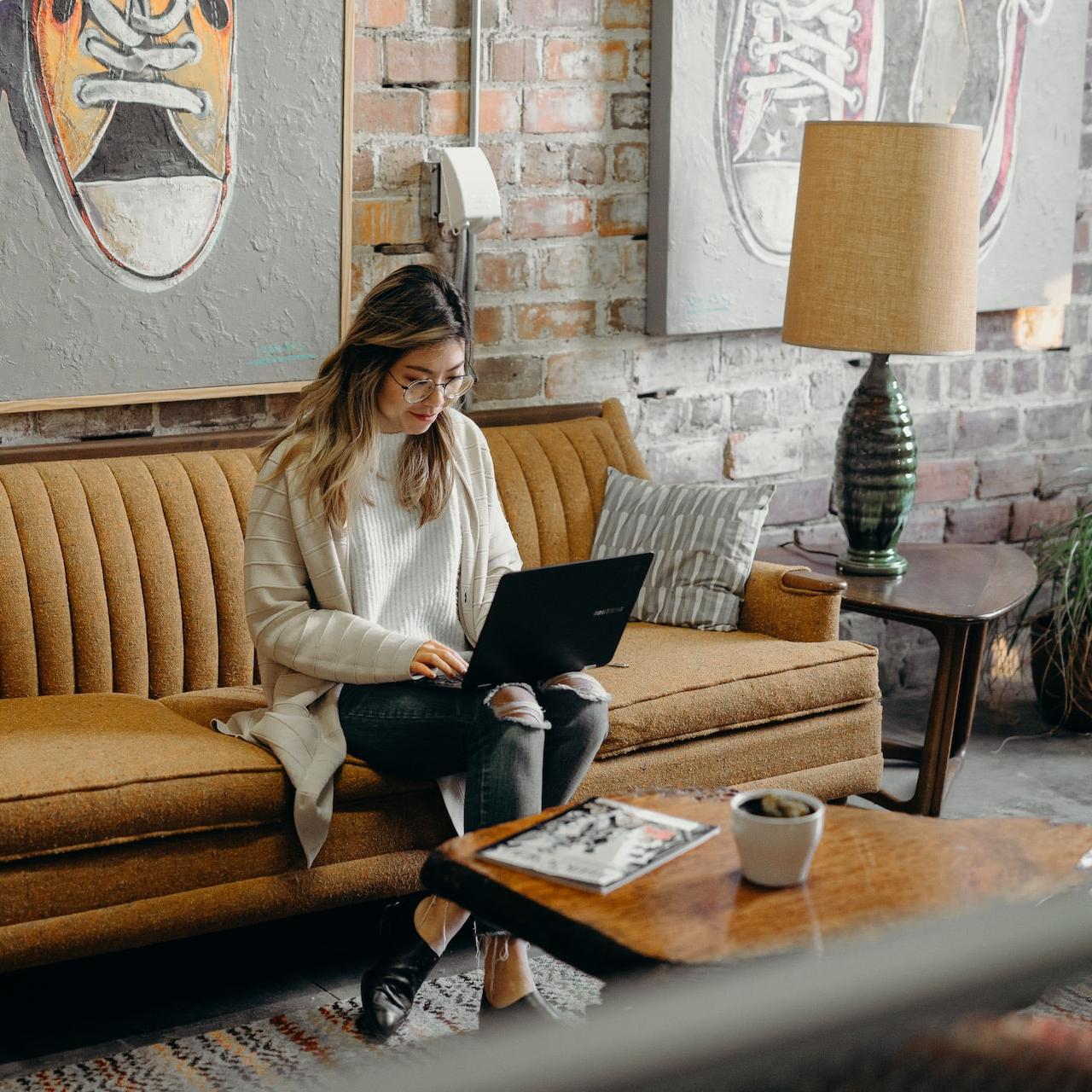 Mujer utilizando una laptop sentada en el sofá de su sala.